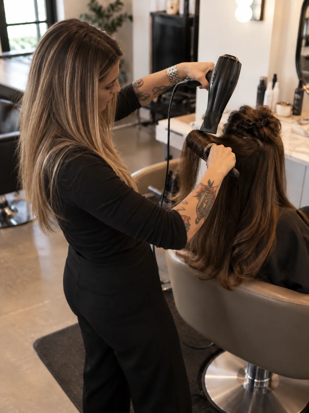 Hair stylist blow-drying a client's hair with a round brush in the salon