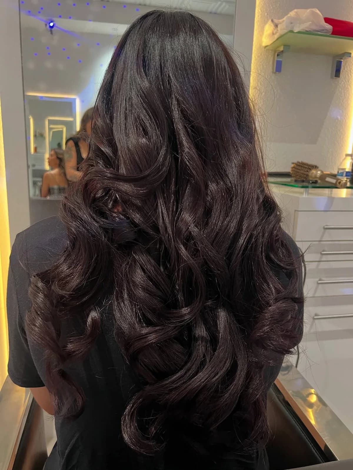 Dark brunette hair with reflective color and flowing curls, photographed from behind in a salon