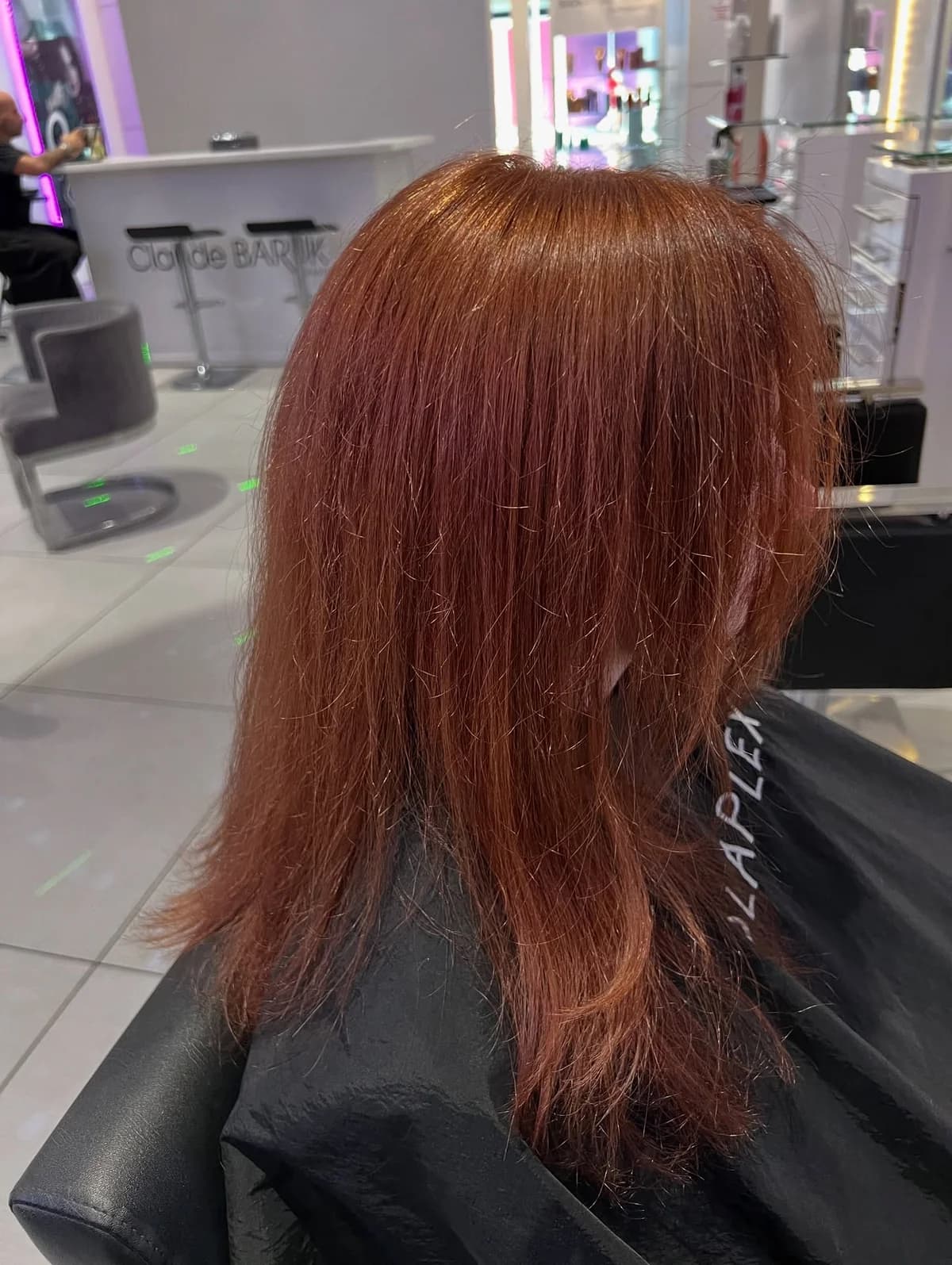 Straight shoulder-length copper hair seen from a rear three-quarter angle in a salon