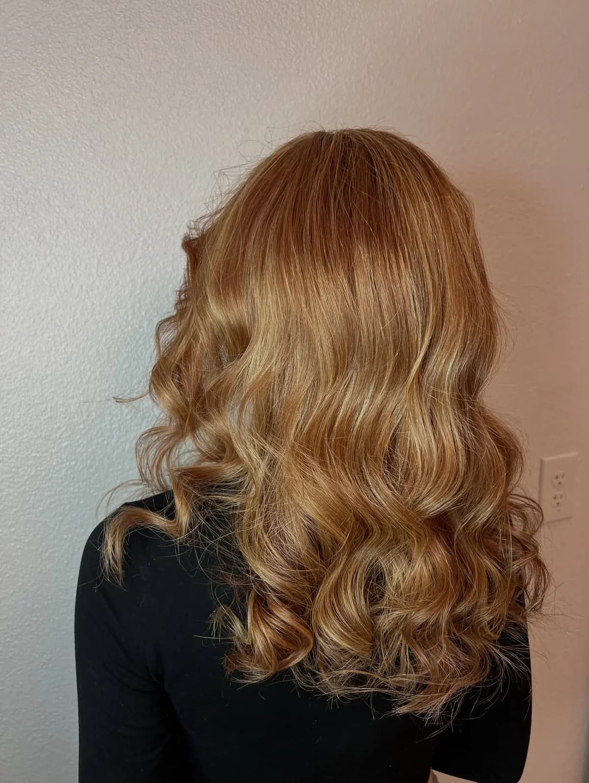 Golden blonde curls seen from behind against a pale wall